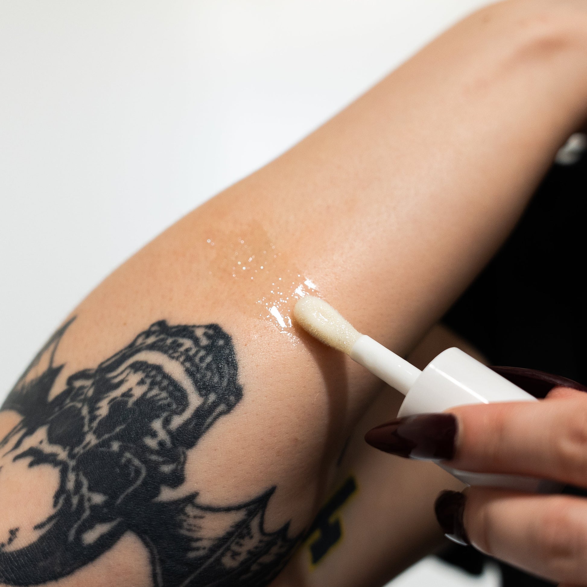 Person applying a white cream or lotion to their arm with a tattoo, against a neutral background.