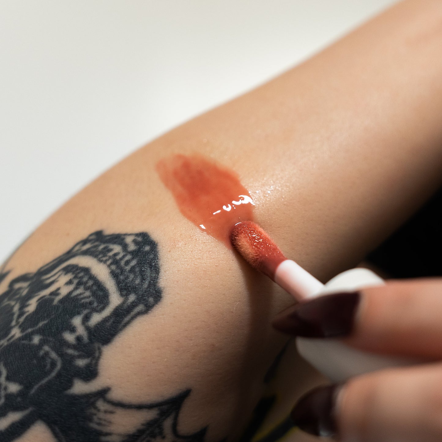 Person applying red lip balm to a tattooed arm