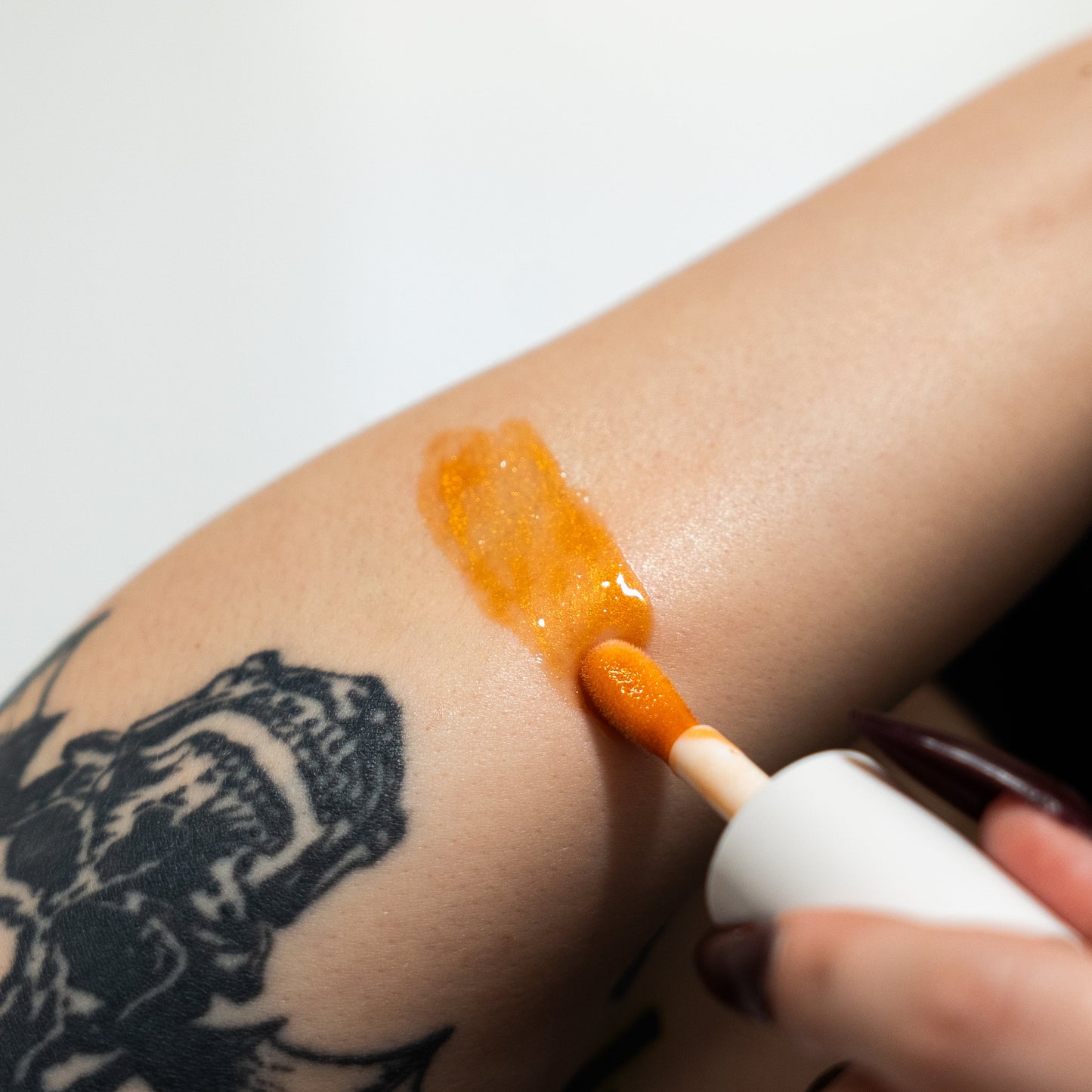 Person applying orange cream to a tattooed arm with a white applicator.