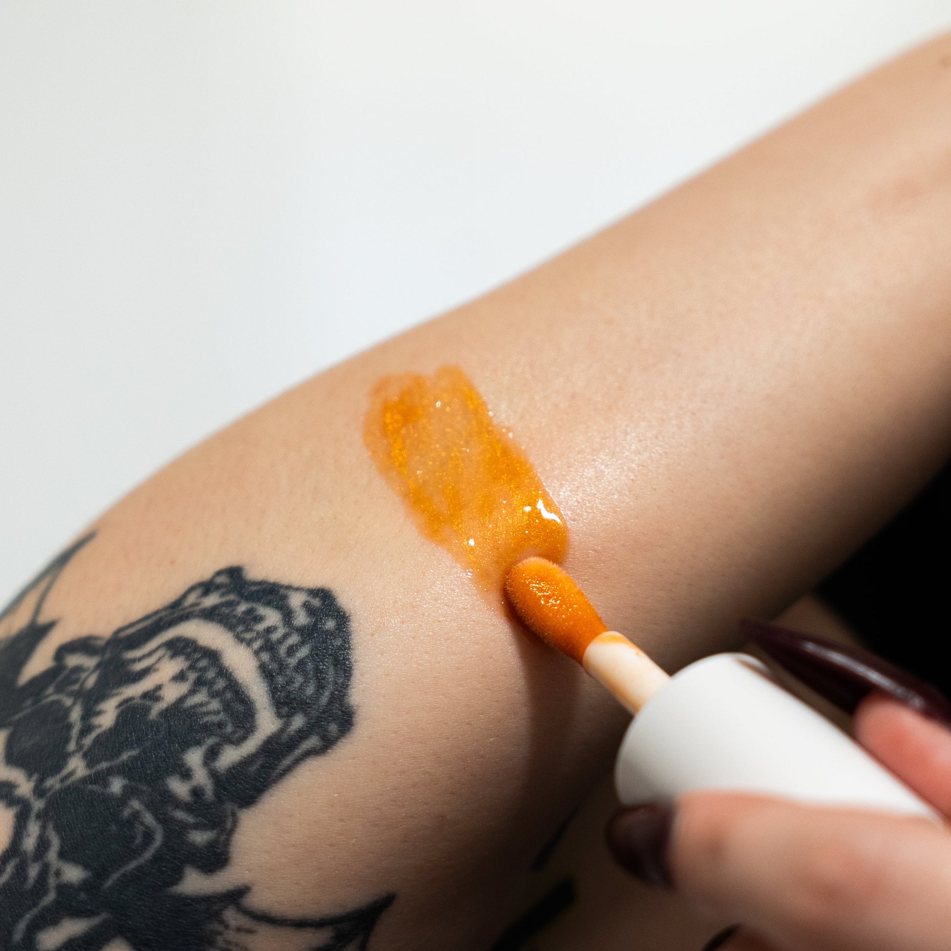 Person applying orange cream to a tattooed arm with a white applicator.