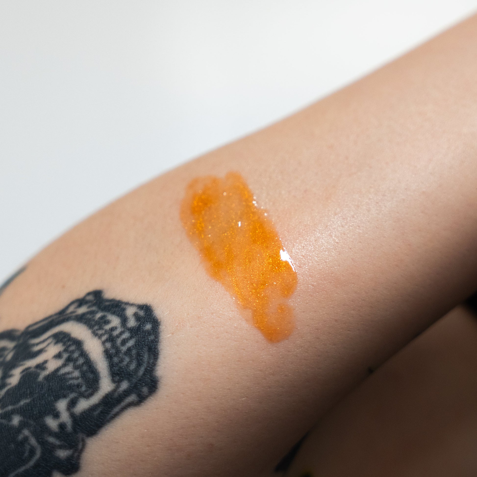 Orange gel or cream swatch on a person's arm with a tattoo in the background