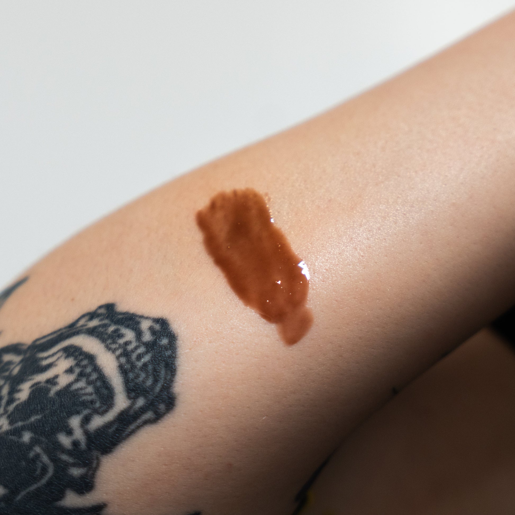 Brown makeup swatch on a person's arm with a tattoo in the background