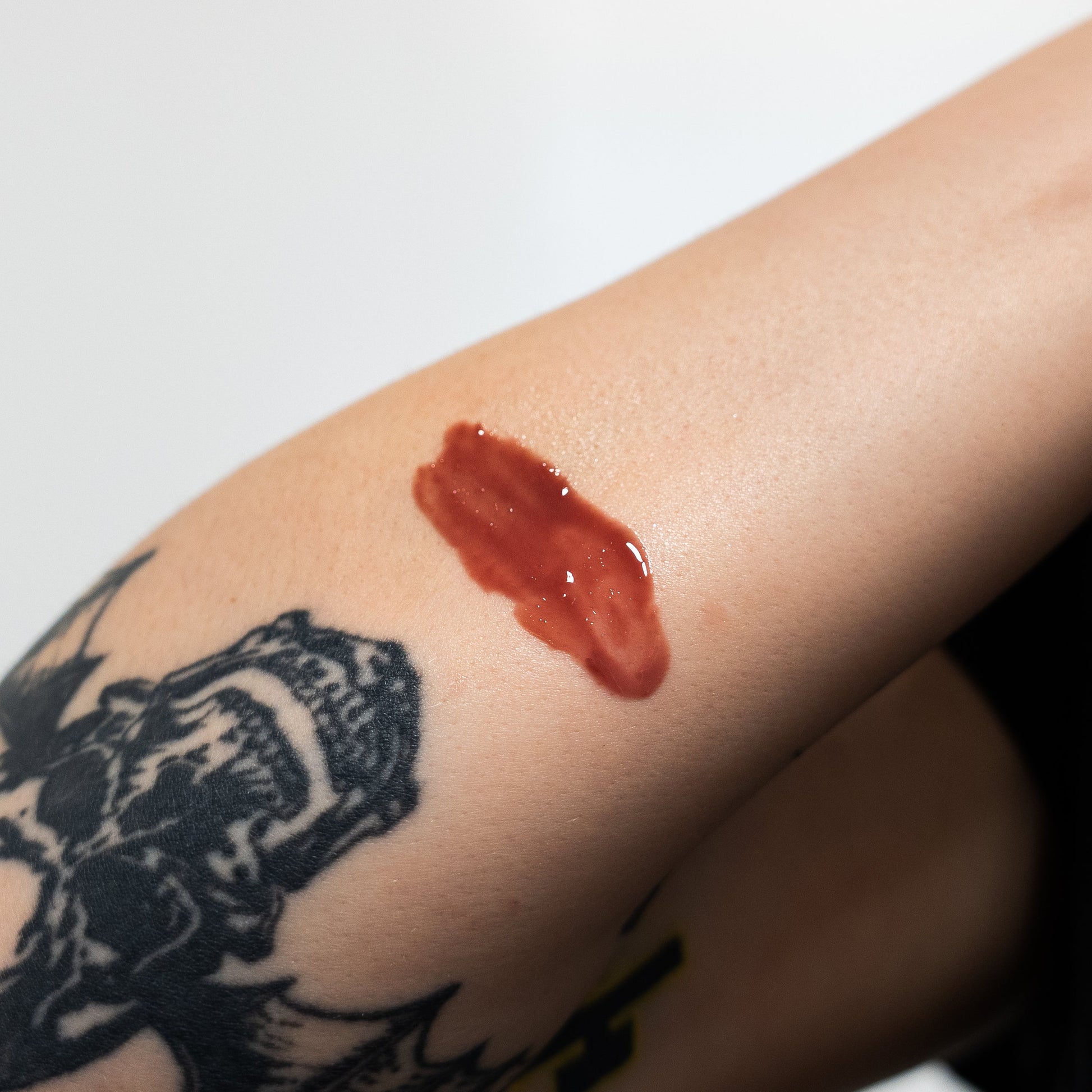 Red substance on a person's arm with a tattoo of a robot, against a white background