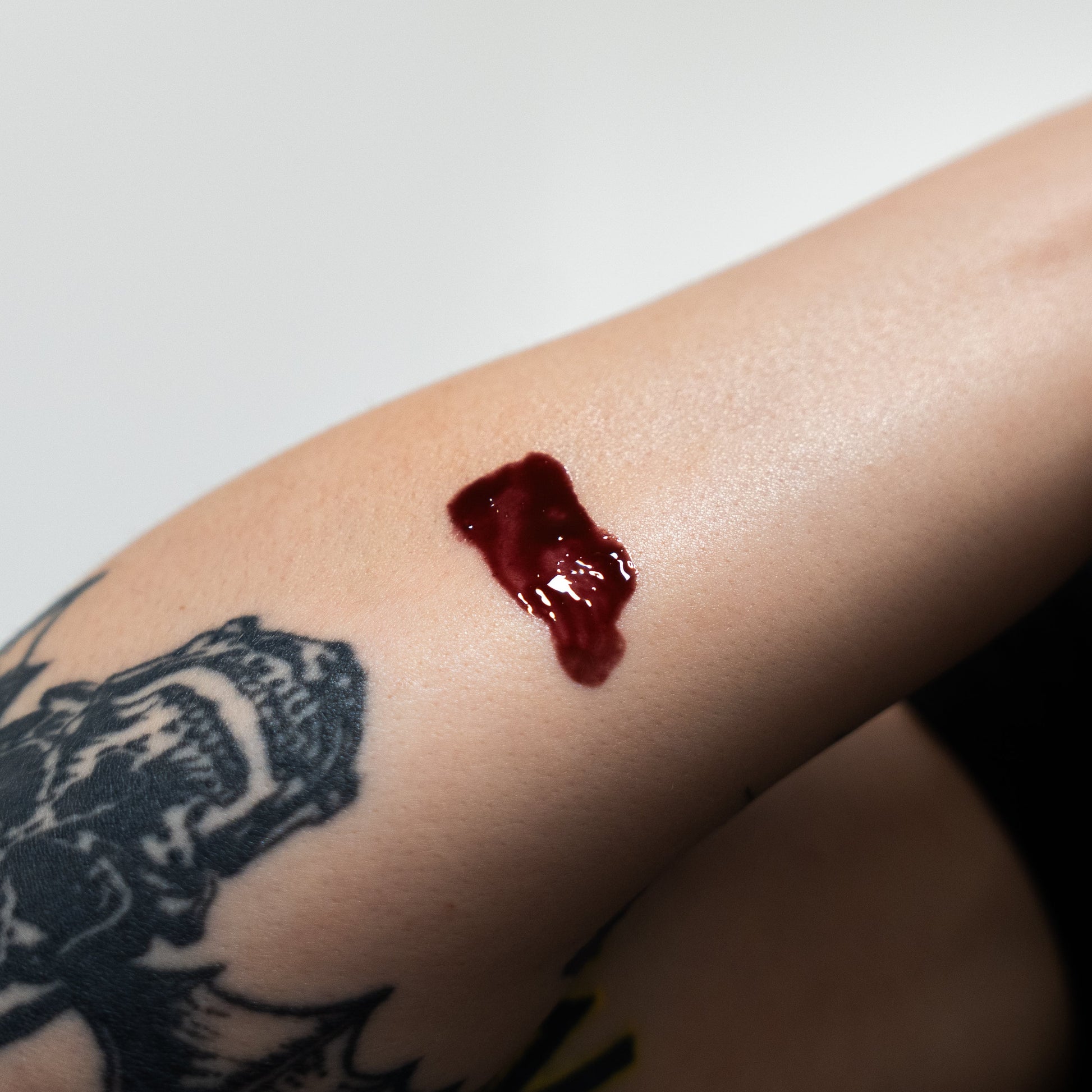 Red gel-like substance on a person's arm with a tattoo in the background