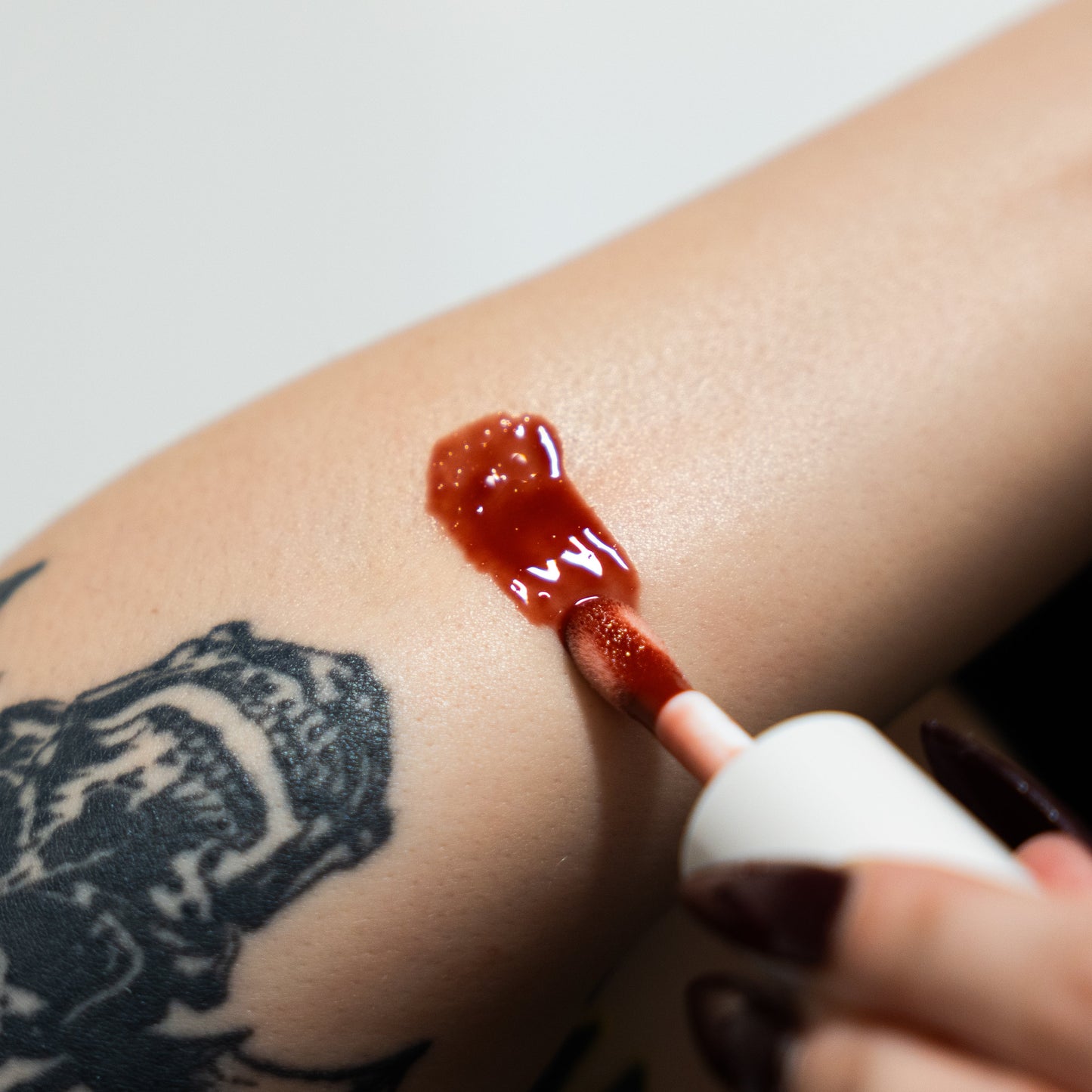 Person applying red lipstick to their arm with a white background