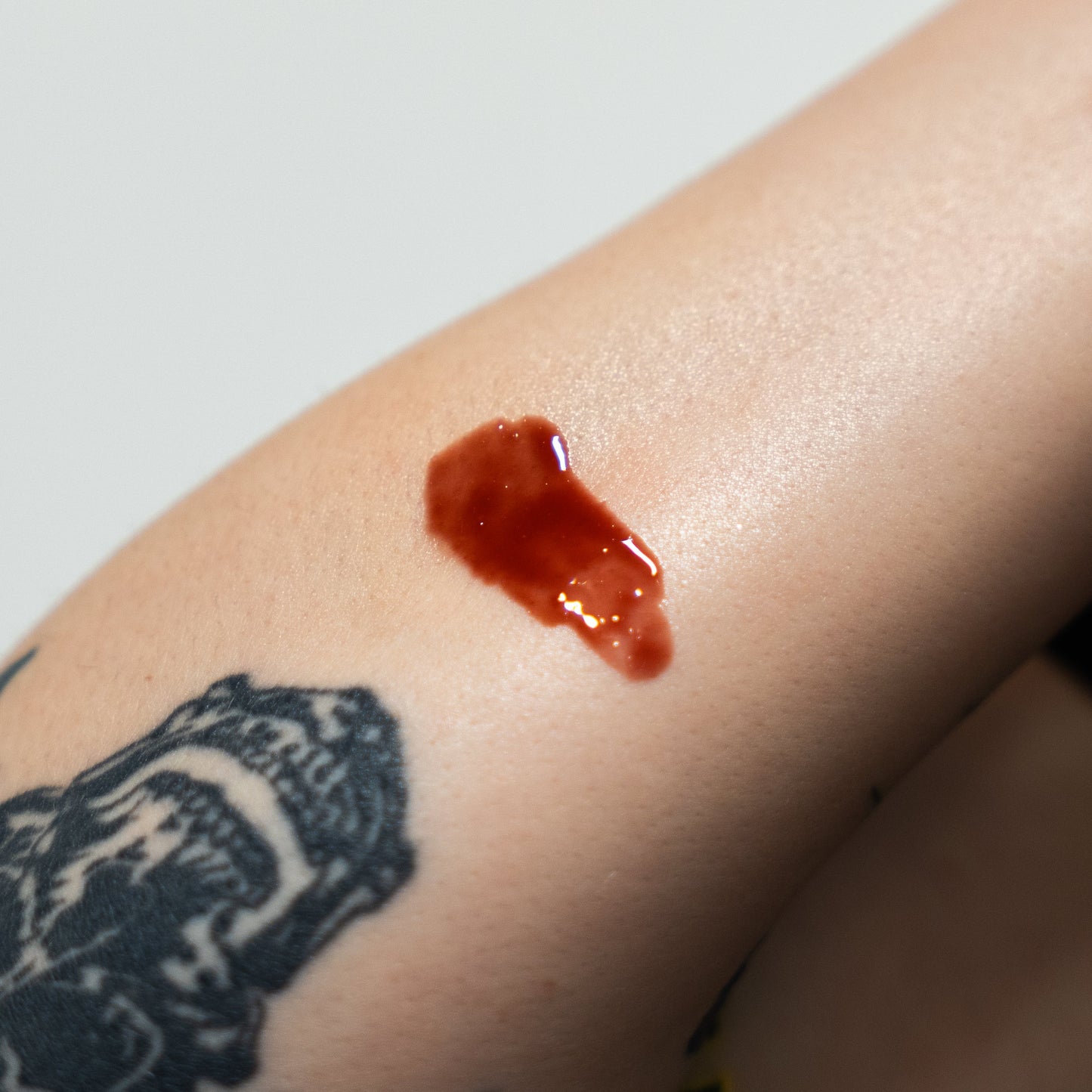 Red liquid stain on a person's arm with a tattoo of a bear paw.