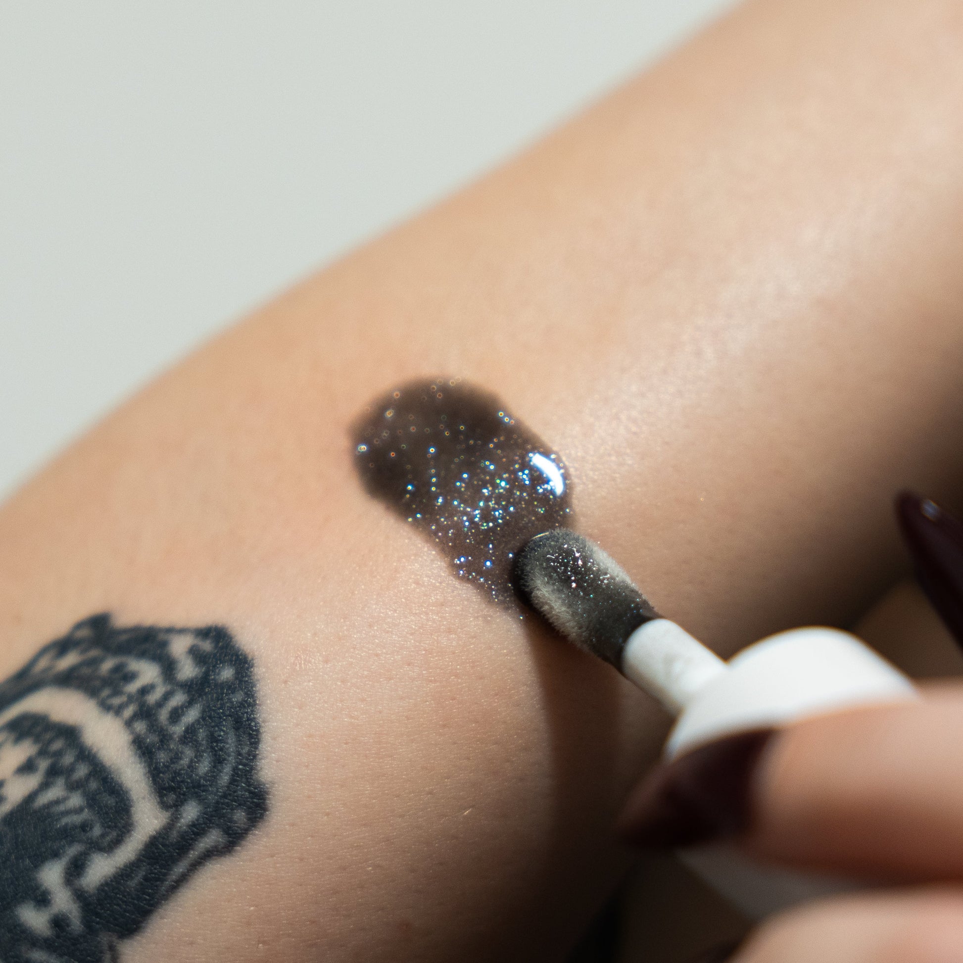 Close-up of a hand applying glittery makeup to a person's arm with a brush.