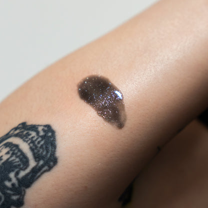 Close-up of a dark glittery substance on skin with a tattoo in the background
